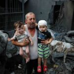A Palestinian refugee carries his injured grandchildren from the Israeli bombing of Nuseirat Camp, Gaza Strip