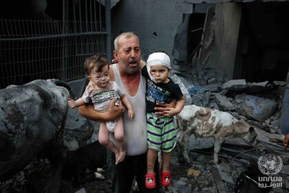 A Palestinian refugee carries his injured grandchildren from the Israeli bombing of Nuseirat Camp, Gaza Strip